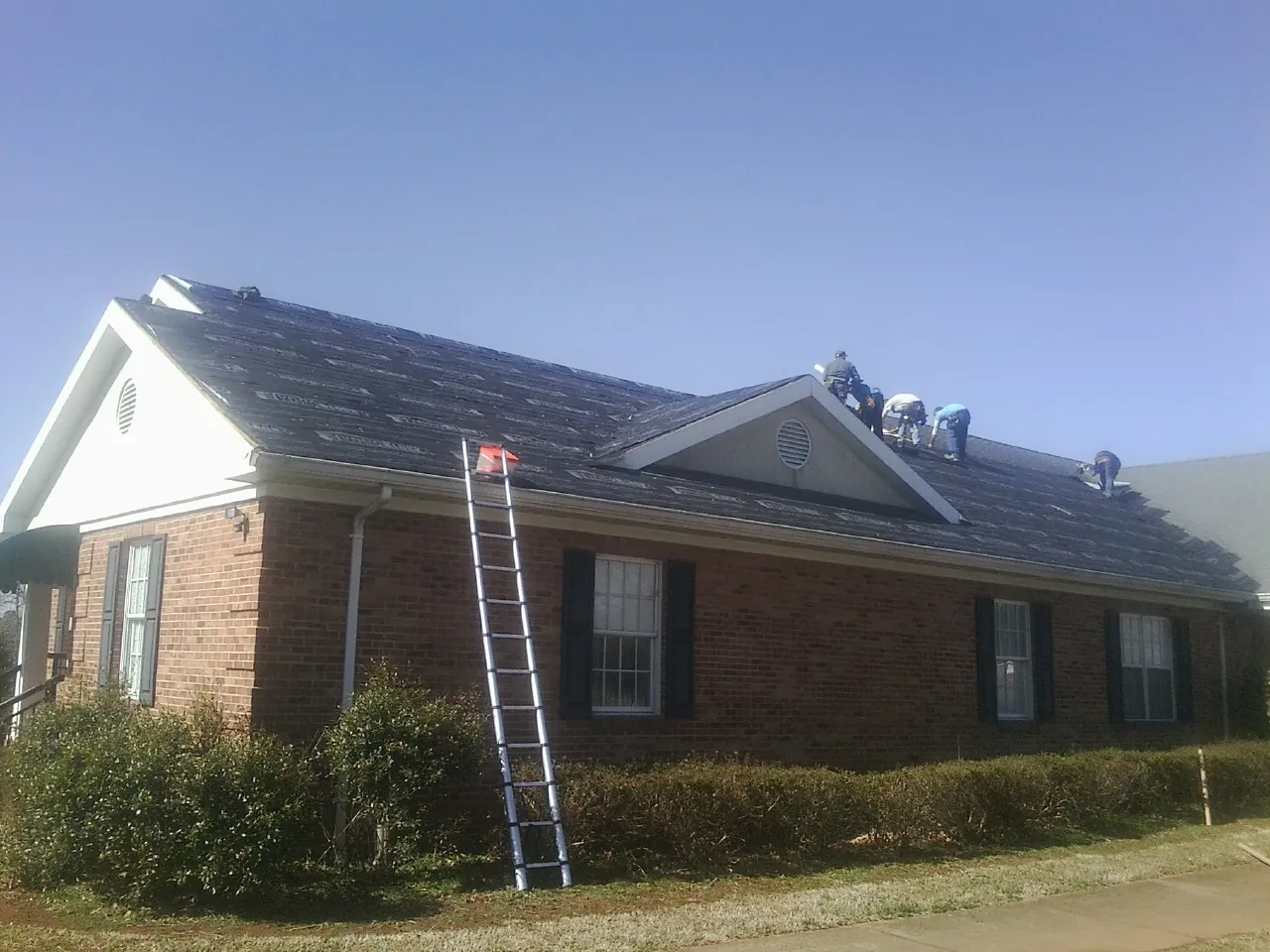 Crew tearing shingles off a brick ranch roof with a ladder set — Metal Roof Repair work by our crew in Belleville