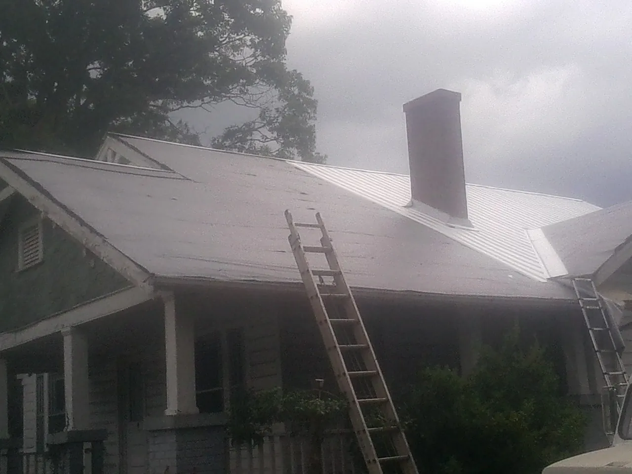 Ladders against a metal roof on an older home with a brick chimney in Belleville