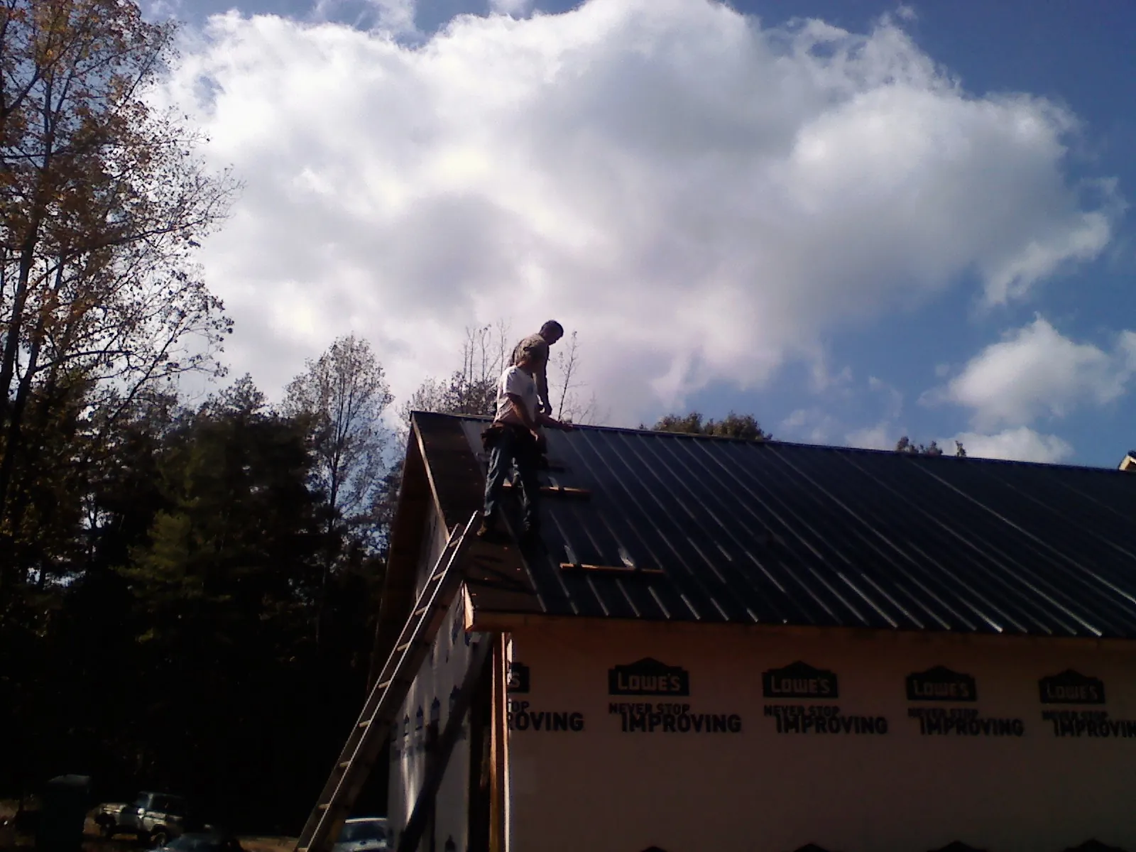 Roofer fastening dark metal panels high against a cloudy sky, from a Roof Inspection job in Belleville